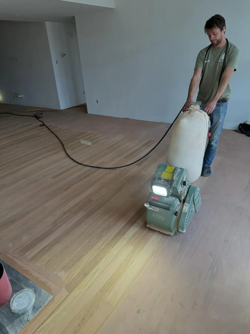 Crew member guiding a drum sander across a hardwood floor during a refinishing job.
