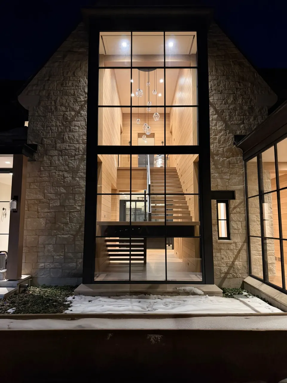 Stone home at night with a lit floating staircase visible through the glass