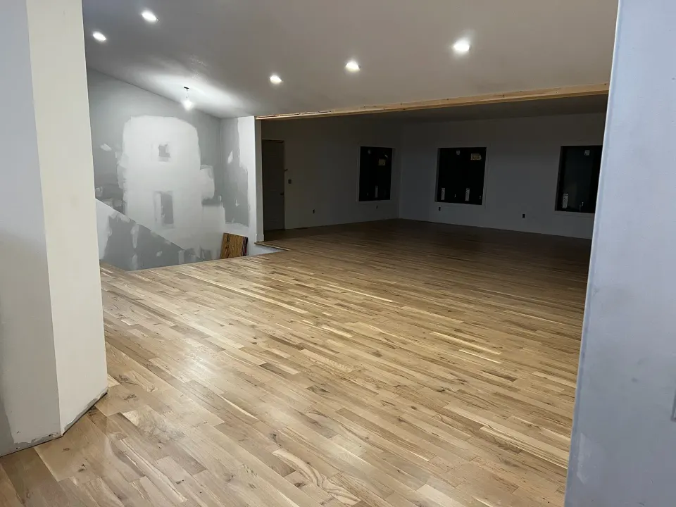 Freshly finished light hardwood floor in an open room still under construction, with unfinished drywall on the walls