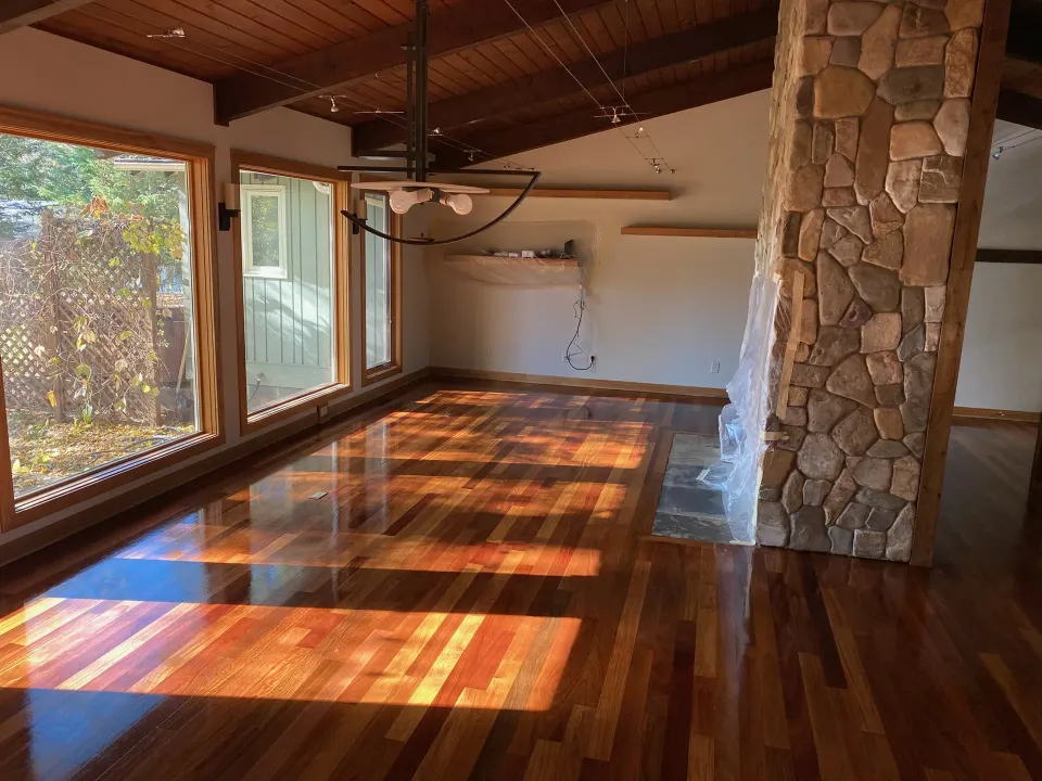 Refinished hardwood floor with a glossy finish in a mid-century living room with a stone fireplace