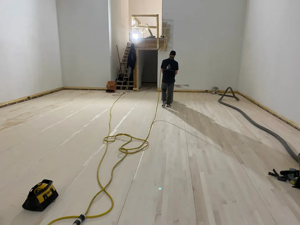 Worker running a sander over raw hardwood flooring before finish